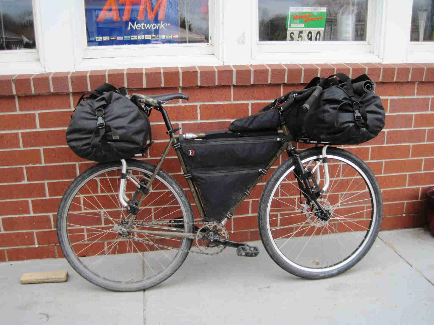 Right side view of a Surly bike, loaded with gear, parked on a sidewalk and leaning against a short brick wall